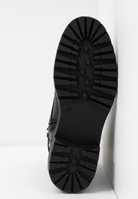 Suela de bota negra con un diseño de banda de rodadura robusto, que presenta surcos profundos y formas puntiagudas. El material parece duradero, adecuado para diversos terrenos.