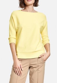 Gul stickad pullover med båtutskärning, trekvartslånga ärmar och ribbad nederkant. Mjuk textur, avslappnad passform och enkel design.