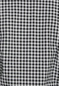 Tissu vichy noir et blanc avec un motif à carreaux, présentant des carrés alternés de petite taille de taille égale et une texture lisse.