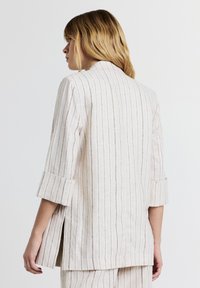 Veste légère en mélange de lin crème avec des rayures verticales. Dotée d'un col, de manches trois-quarts, d'une fente sur les côtés et d'une coupe décontractée.