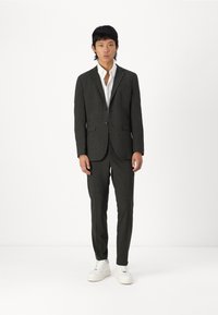 Costum în carouri închise cu sacou croit și pantaloni slim-fit, asortat cu o cămașă albă și teniși albi. Design simplu și modern.