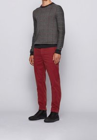 Szary dzianinowy sweter w kratkę z czarnym ściągaczem, w połączeniu z czerwonymi sztruksowymi spodniami i czarnymi wysokimi trampkami. Prosty, codzienny strój.