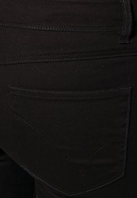 Svarta denimjeans med en slät yta, som har en enda bakficka med diskret sömnadsdetalj och böjda designelement.