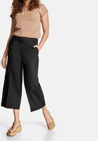 Kortärmad tröja i tan med texturerad "hej"-detalj, matchad med svarta vida byxor och beige plattformsandaler med ankelremmar.