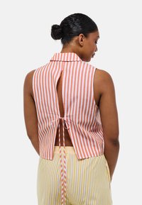 Une blouse sans manches avec col présente des rayures orange et blanches, un dos en trou de serrure avec un lien de fermeture, et un tissu léger pour le confort.