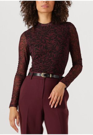 Mouwenlange top in donker bordeaux met een bladerenpatroon, gemaakt van doorschijnende stof, gecombineerd met hoog-waisted bordeaux broek en een zwarte riem.
