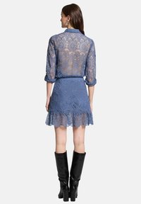 Robe en dentelle bleue avec des manches longues, un corsage ajusté et une jupe évasée avec un ourlet festonné. Assortie à des bottes noires montantes.