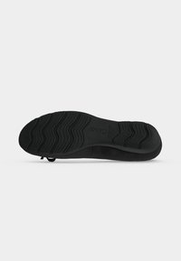 Semelle de chaussure noire avec motif ondulé, nom de la marque visible au centre, affichée sur un fond gris clair uni.