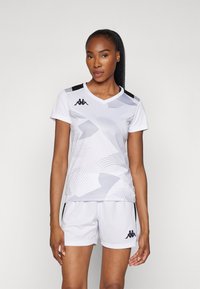 Hvit sportsdrakt med grå grafiske mønstre, V-hals, og svarte detaljer. Kombinert med hvite shorts med svart logo på kanten.