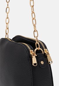 Sort lædertaske med en struktureret overflade, prydet med hardware i guld-tone, dobbelte lynlåse og en metallisk kædestrop.