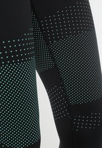 Leggings sportivi neri con un motivo testurizzato di piccoli triangoli turchesi, caratterizzati da un tessuto liscio e dettagli di cucitura a contrasto.