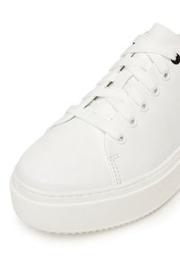 Sneakers din piele albă cu vârful rotund, talpă plată din cauciuc și șireturi plate. Caracterizate prin cusături minime și o suprafață netedă, concepute pentru purtare casual.