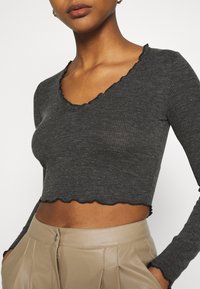 Ciemnoszary prążkowany krótki top z długim rękawem, ozdobiony falistym dekoltem i wykończeniem, zestawiony z beżowymi spodniami z wysokim stanem.