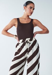 Brown ribbed tank top paired with high-waisted, wide-leg pants featuring bold brown and cream diagonal stripes and an adjustable waistband.