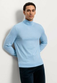 Hellblaues Rollkragensweatover aus weichem Stoff. Figürliches Design mit langen Ärmeln und gerippten Bündchen. Getragen über navyblauen Cordhosen.