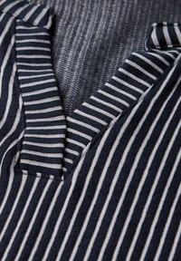 Marinblå och vit randig tyg med V-halsdesign. Texturerad stickning med en blandning av breda och smala ränder. Ren finish på kragens kanter.