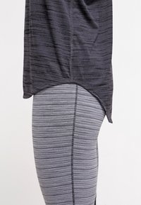 Zwart sporttopje met een gestructureerd patroon, gecombineerd met grijze gestreepte leggings met een vlakke naad en elastische tailleband.