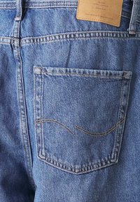 Vaqueros de mezclilla de color azul clásico. Presentan un bolsillo trasero con un detalle de costura curvada y una etiqueta de cuero encima, lo que enfatiza su durabilidad.