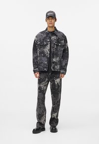 Τζάκετ από τζην και ψηλοκάβαλο παντελόνι σε μαύρο χρώμα με γκρι αφηρημένα σχέδια. Το σύνολο έχει χαλαρή εφαρμογή, κουμπιά μπροστά και μαύρα slip-on παπούτσια.