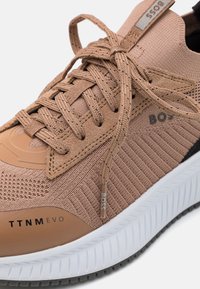 Gros plan d'une basket de couleur beige en tissu tricoté texturé, lacets noués, marque BOSS, et une semelle blanche texturée.