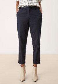 Námořnické modré, vhodně střižené kalhoty s ohrnutým lemem, bočními kapsami a černým opaskem. Spárováno s béžovými, špičatými kotníkovými botami.