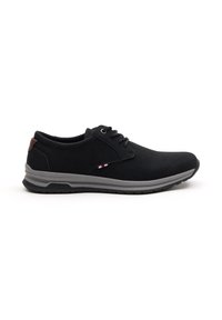Zapatos casuales negros con una parte superior texturizada, suela de goma gris y acento marrón en el talón; cuentan con un diseño de cordones y detalles de color sutiles.