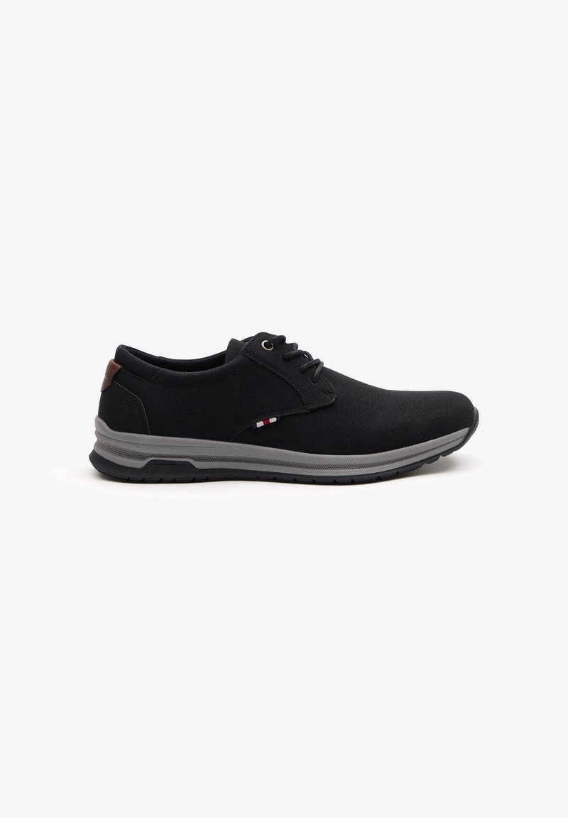 Zapatos casuales negros con una parte superior texturizada, suela de goma gris y acento marrón en el talón; cuentan con un diseño de cordones y detalles de color sutiles.