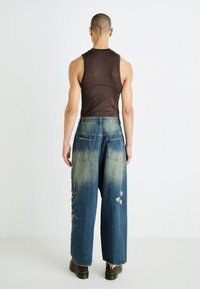 Top marrón sin mangas y vaqueros de pierna ancha desgastados con detalle de cuentas en el lateral, con una pretina alta y acentos desgastados.