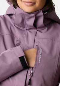 Ljuslila jacka med hög krage, blixtlåsförsedd bröstficka, kardborreförsedda ärmslut och broderad logotyp, tillverkad av slätt tyg.