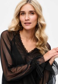 Czarna, przejrzysta bluzka z długimi, luźnymi rękawami, koronkowym wykończeniem wokół dekoltu oraz zebranymi mankietami. Tekstura jest lekka i przezroczysta.