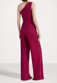 Yksipuoleinen haalari syvässä burgundin värissä, jossa on istuva yläosa ja leveät, hulmuavat lahkeet. Valmistettu sileästä, venyvästä kankaasta.