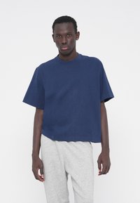 Μπλε ναυτικό κοντό t-shirt από απαλό βαμβακερό ύφασμα, με στρογγυλή λαιμόκοψη και κοντά μανίκια, σε συνδυασμό με γκρι φόρμα.