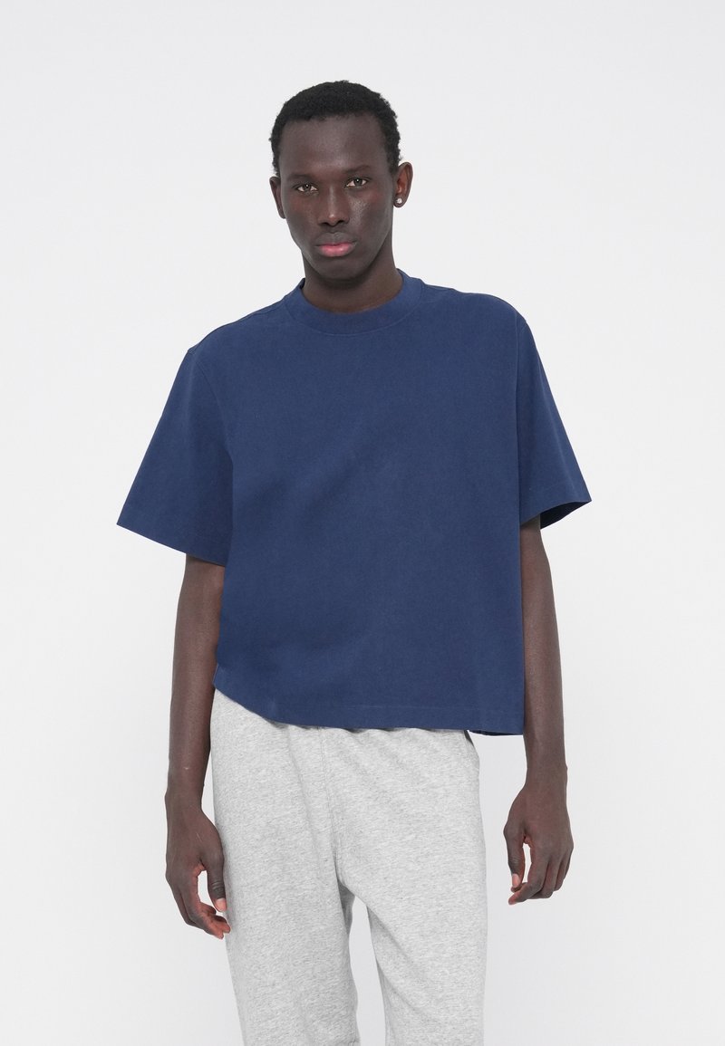 Μπλε ναυτικό κοντό t-shirt από απαλό βαμβακερό ύφασμα, με στρογγυλή λαιμόκοψη και κοντά μανίκια, σε συνδυασμό με γκρι φόρμα.