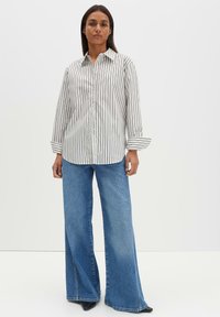 Gestreiftes Hemd mit Knöpfen in Weiß und Schwarz, kombiniert mit weit geschnittenen blauen Jeans. Baumwollmaterial, entspannte Passform, lange Ärmel, mit Manschetten am Handgelenk.