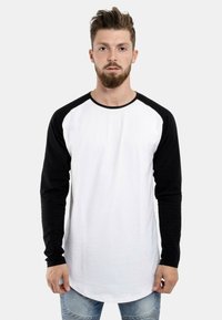 Langärmliges Raglan-Shirt mit einem schwarz-weißen Farbschema. Weißer Körper, schwarze Ärmel, lockere Passform und abgerundeter Saum. Aus Baumwolle gefertigt.