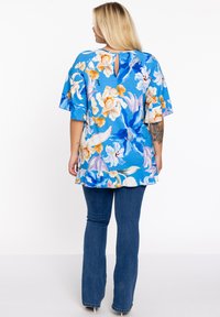 Blauw bloemen tuniek met korte, uitlopende mouwen en een sleutelgatsluiting aan de achterkant. Heeft levendige oranje en witte bloemen tegen een blauwe achtergrond.