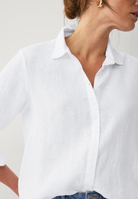 Camicia di lino bianca con design a bottone, colletto e maniche arrotolate. Tessuto liscio con una vestibilità casual. Presenta una patta con bottoni.