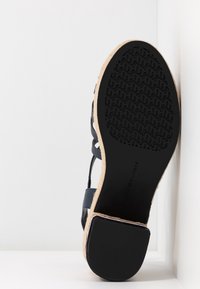 Černé sandály s texturovanou gumovou podešví a korkovým mezipodešví. Mají křížově uspořádané kožené popruhy a nízký podpatek.