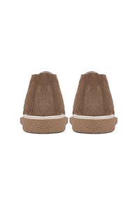 Paire de chaussures en daim marron vues de dos avec semelles en caoutchouc beige texturé et coutures blanches sur les bords.