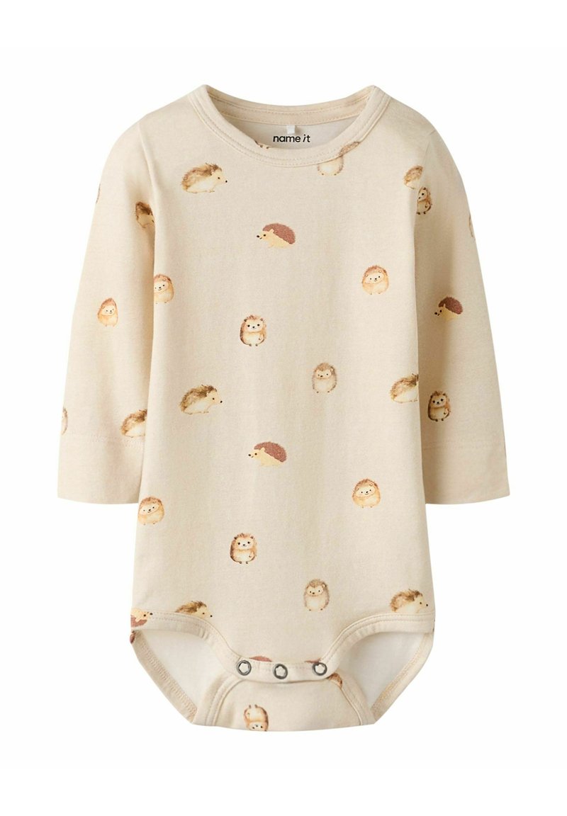Body z długim rękawem w jasnobeżowej bawełnie z powtarzającym się nadrukiem jeża. Posiada zapięcie na napy na dole. Miękka, gładka struktura.