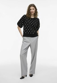 Melnā adītais džemperis ar baltiem punktiņiem, kombinēts ar gaiši pelēkiem piegrieztiem biksēm un melniem zābakiem ar papēdi. Vienkāršs un strukturēts dizains.