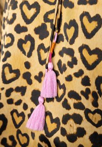 Leopard print fabric in beige and black, featuring heart-shaped patterns. Two pink tassels hang from a narrow, dark cord.