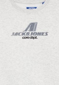 Sudadera gris claro con cuello redondo. Presenta un logo impreso en azul oscuro "JACK & JONES" y "core dept." en negro debajo. Textura suave.