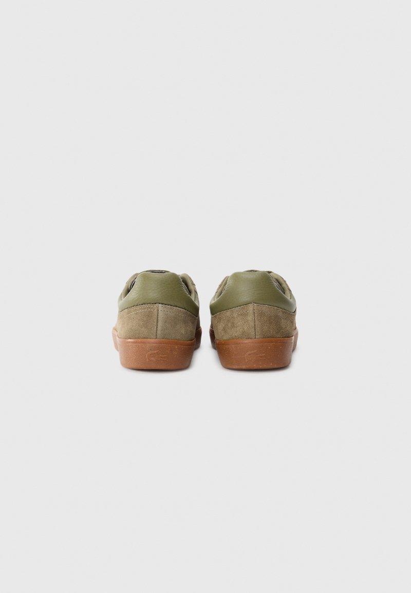 Une paire de baskets basses en suède olive et marron, vue de l'arrière sur un fond blanc uni.