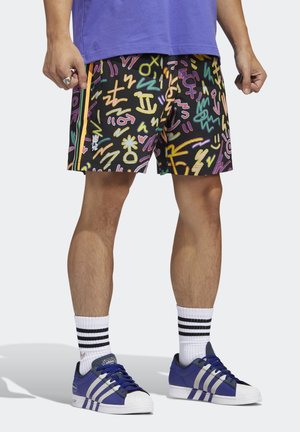 Färgglada shorts med abstrakta mönster i rosa, gult och blått på svart bakgrund, kombinerade med blå skor och vita strumpor med ränder.