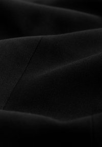 Černá látka s hladkou texturou, představující jemné hrbolky a záhyby. Materiál se jeví jako hustě tkaný a odolný.