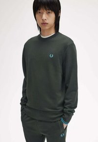 Sudadera de color verde oscuro con cuello y puños acanalados, que presenta un pequeño logo bordado azul en el pecho y pantalones de color verde oscuro a juego.