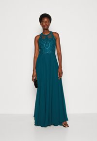 Rochie de seară teal, cu un corset ajustat și embellisat și o fustă fluidă. Prezentând mărgeluțe intricate și detalii din dantelă pe piept.