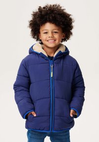 Granatowa kurtka ocieplana z teksturowanym wykończeniem, kontrastowe niebieskie zamki błyskawiczne oraz beżowy kaptur wykończony futrem. Dwie przednie kieszenie i luźny krój.