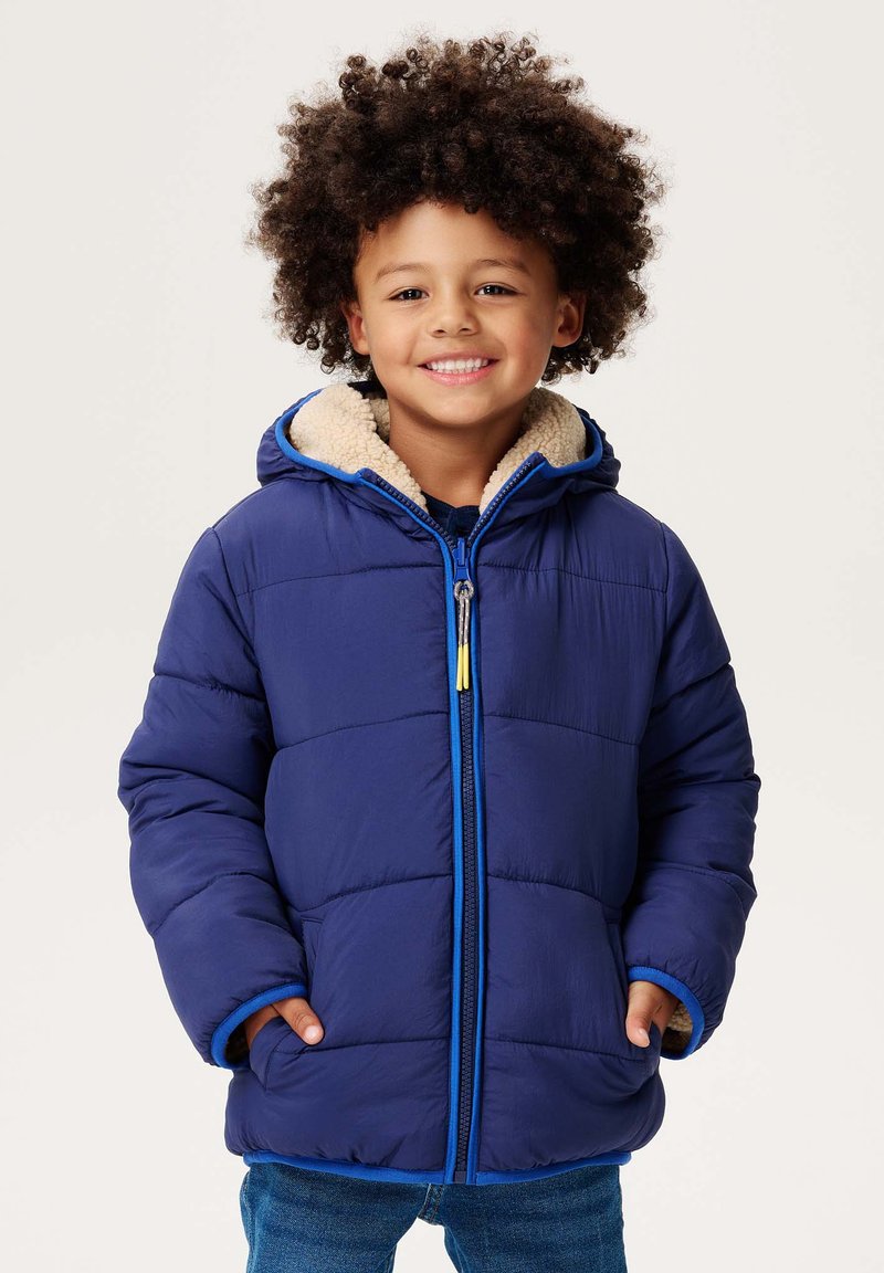Granatowa kurtka ocieplana z teksturowanym wykończeniem, kontrastowe niebieskie zamki błyskawiczne oraz beżowy kaptur wykończony futrem. Dwie przednie kieszenie i luźny krój.